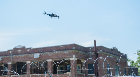 a Skydio X10 drone over a building surrounded by razor wire fence