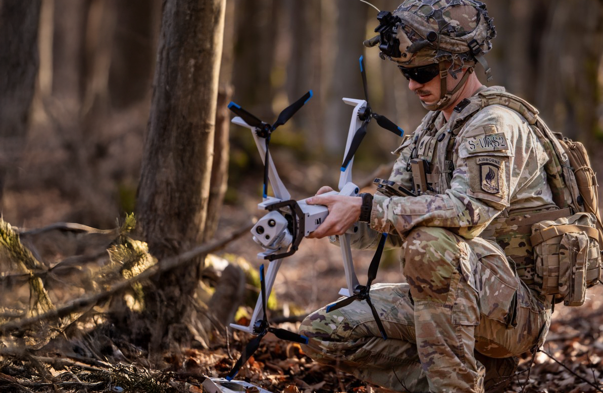 crouching warfighter in the woods with a Skydio X10D drone in hand